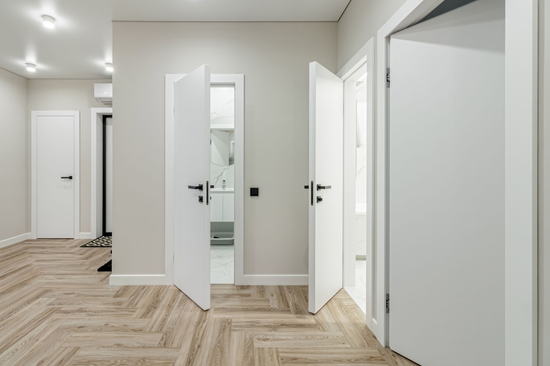 White entrance door in a modern renovated hallway with large mirrors and wardrobe